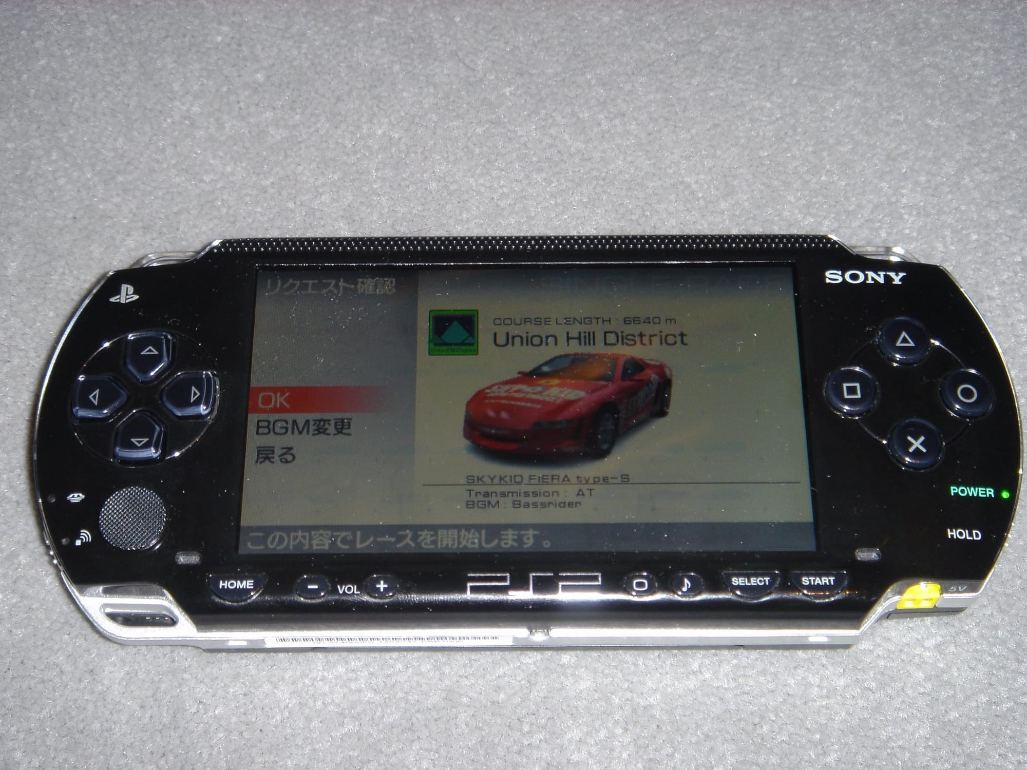 A photo of a PlayStation Portable, with the game Ridge Racers displayed on the screen.