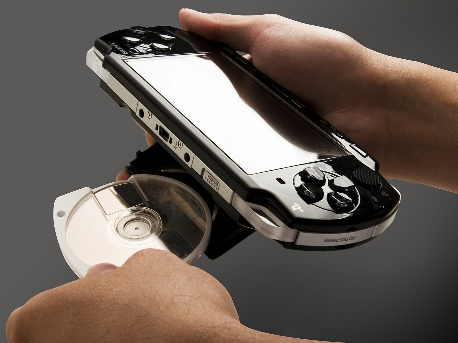 A photo of someone sliding a UMD disc into the back of a PlayStation Portable.