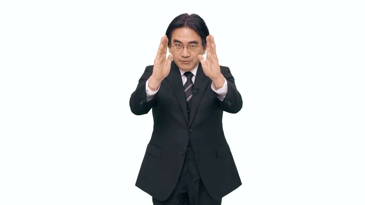 Late Nintendo CEO Satoru Iwata making a hand gesture during a Nintendo Direct broadcast.